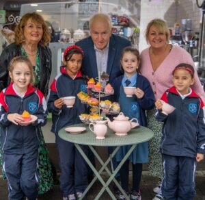 Picture of Listowel Food Fair committee members, at a cafe table, with local school children, each holding tea cups